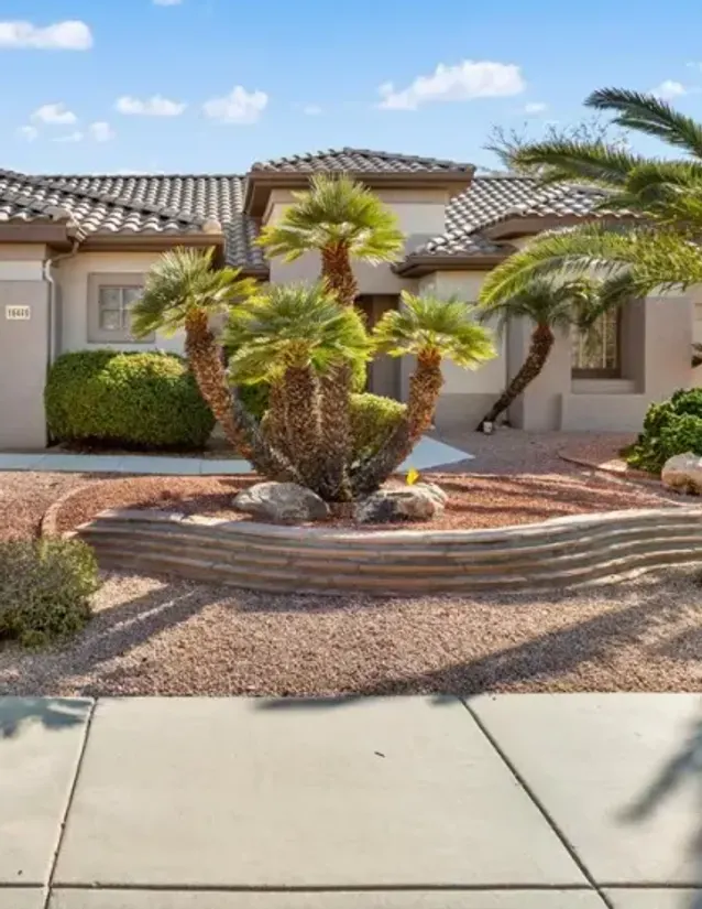 Gravel front yard with a stacked stone planter and palm trees at a Sun City Grand home